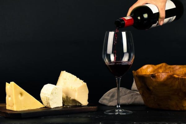 Red wine being poured into glass next to cheese board