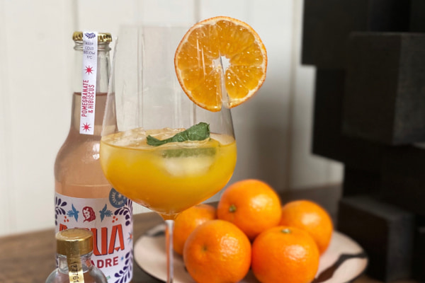Bottle of Agua de Madre by an orange cocktail