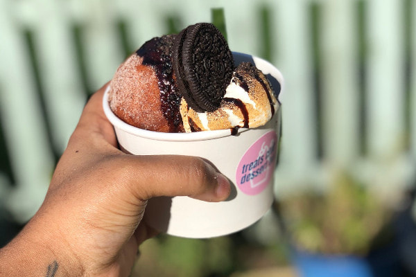 hand holding out a donut sundae in a paper tub